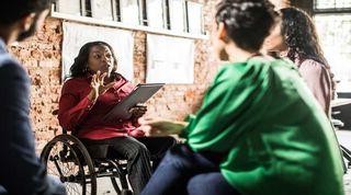 Woman in a wheelchair presents from a tablet to a group of people 